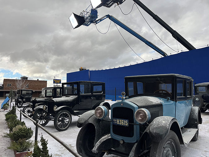 1920s era cars used in the filming of “1923” line the front of the train depot in Butte, Montana. The blue backdrop and lights behind them block the cars from public view on Front Street.